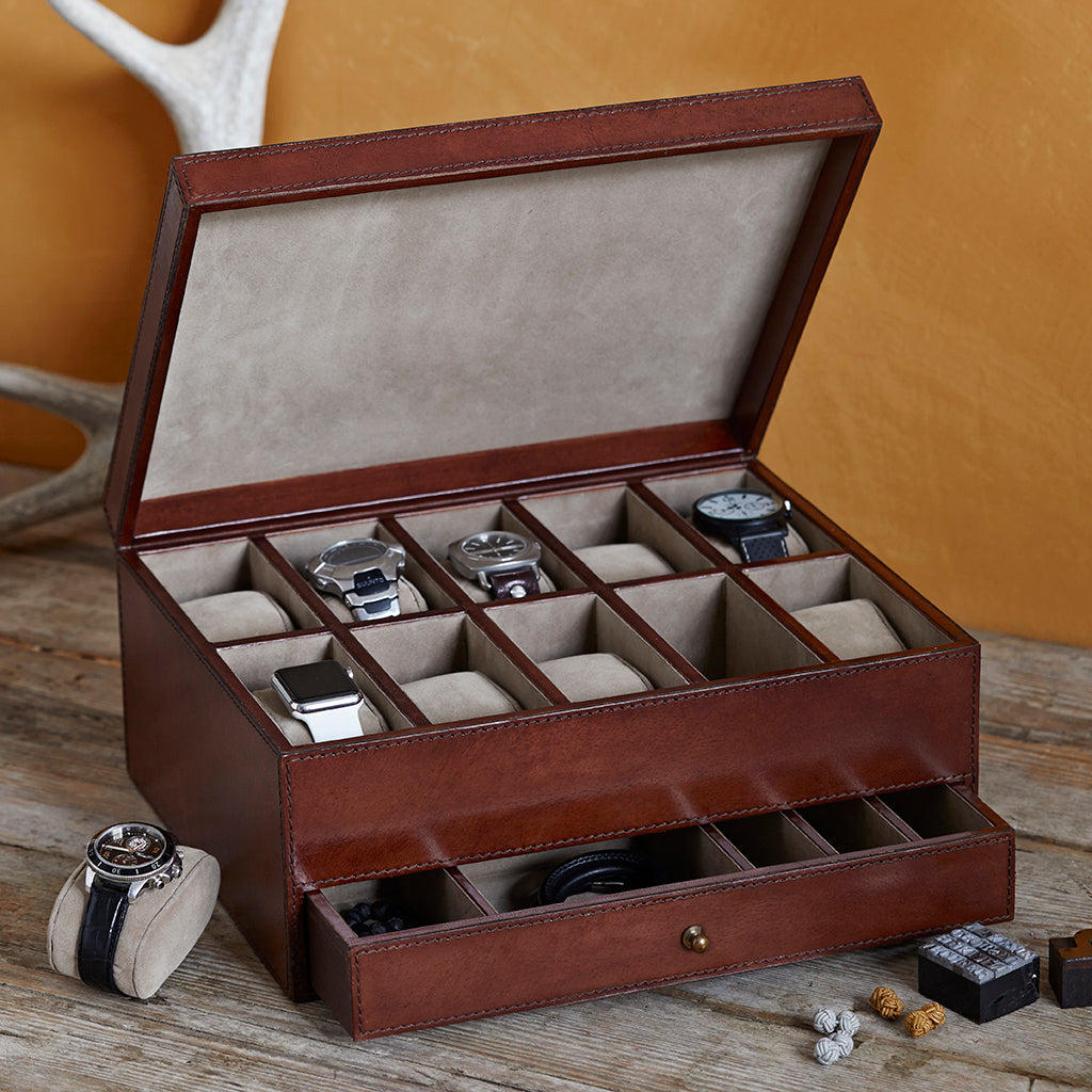 A leather watchbox showing multiple watch slots and a drawer, styled on a wooden surface with watches and accessories.