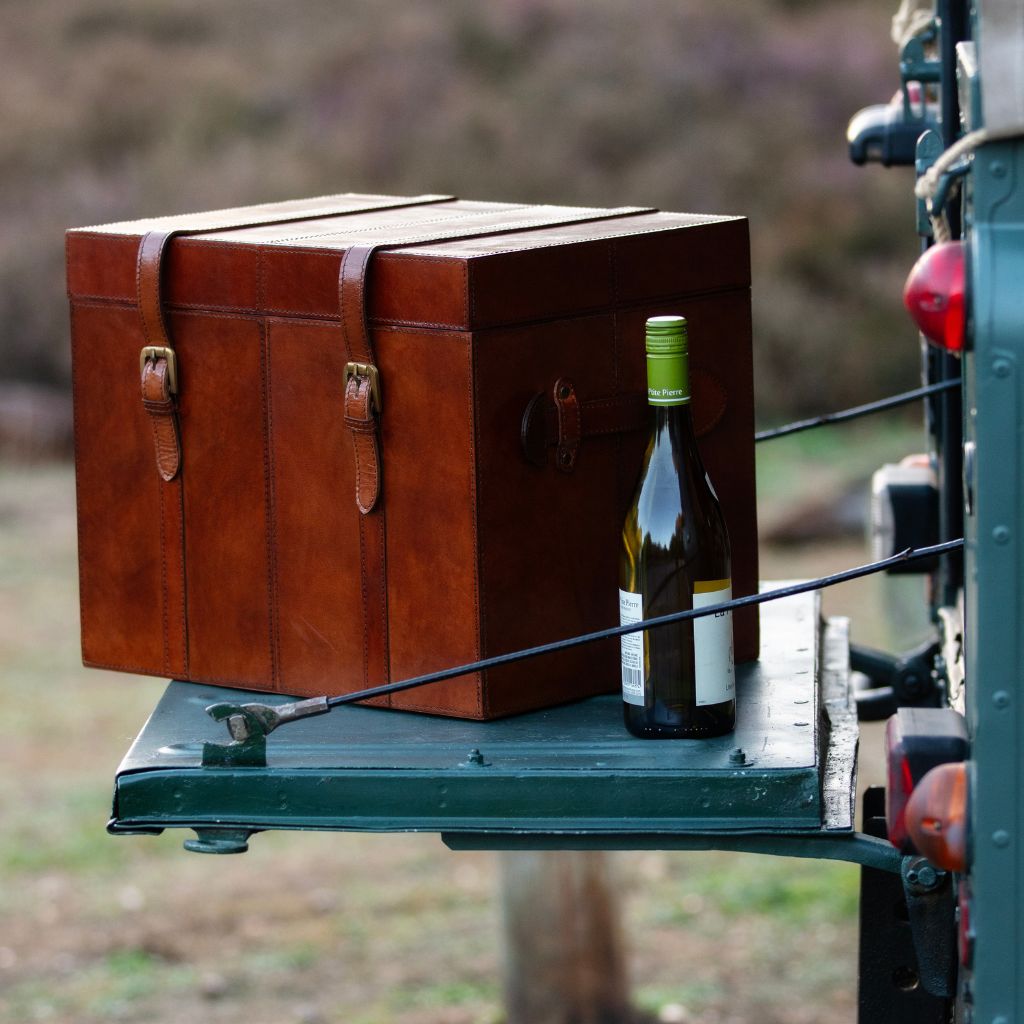 Leather champagne trunk to fit six bottles shown closed on the tailgate of a landrover with a cottle of wine to the side