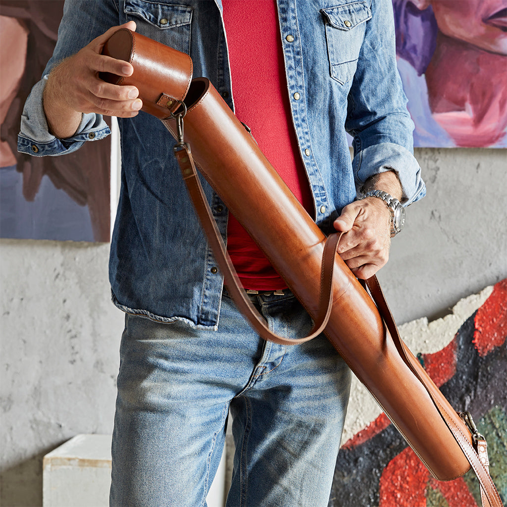 Man holding a the leather strap of the leather cylinder map document case, and removing the lid of the case