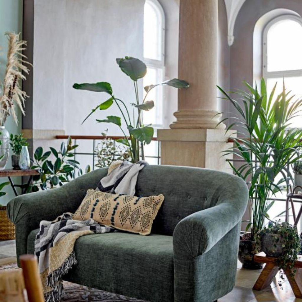 Green sofa with decorative pillows in a room with large windows and plants