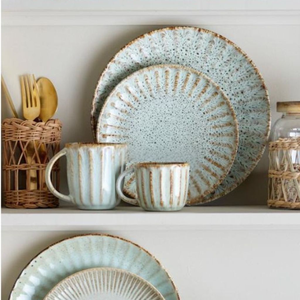 Speckled green and brown ceramic dinnerware set on a white surface with wicker baskets.