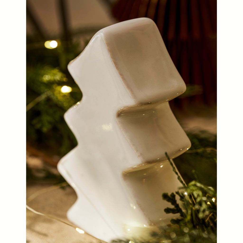 Decorative white ceramic tree-shaped object on a reflective surface with blurred background