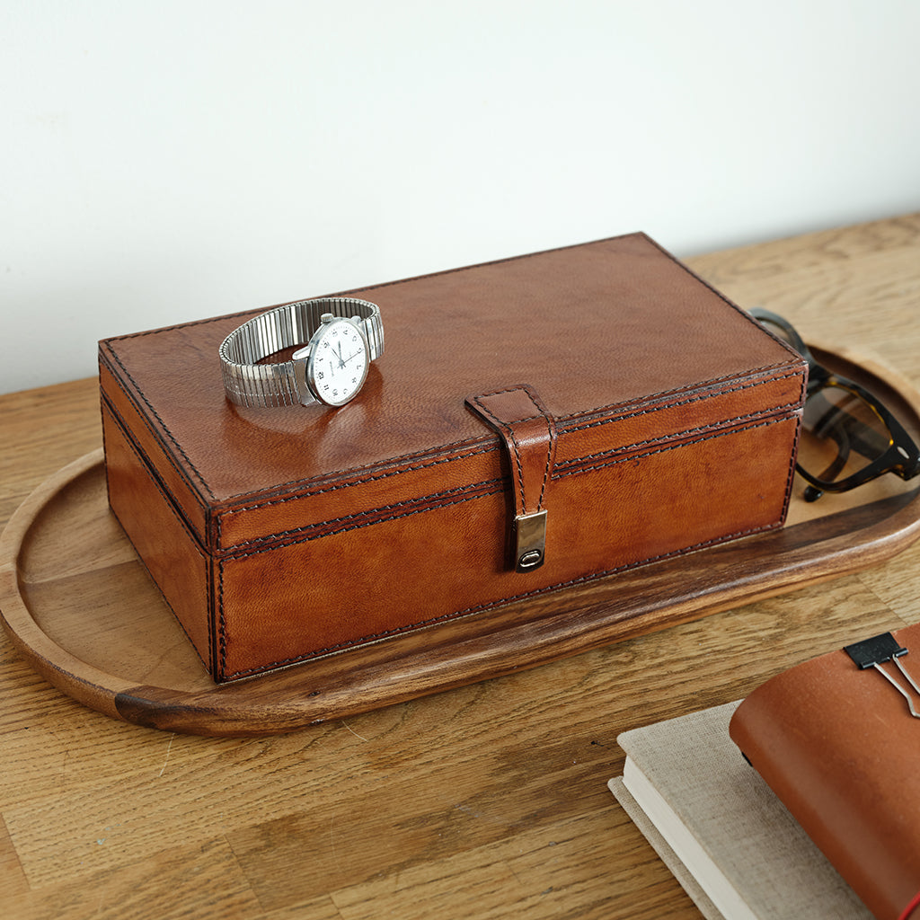 Brown leather jewellery box with a watch on a wooden surface