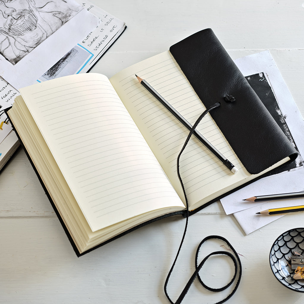 Open notebook with a black leather cover and a pencil on a white surface.