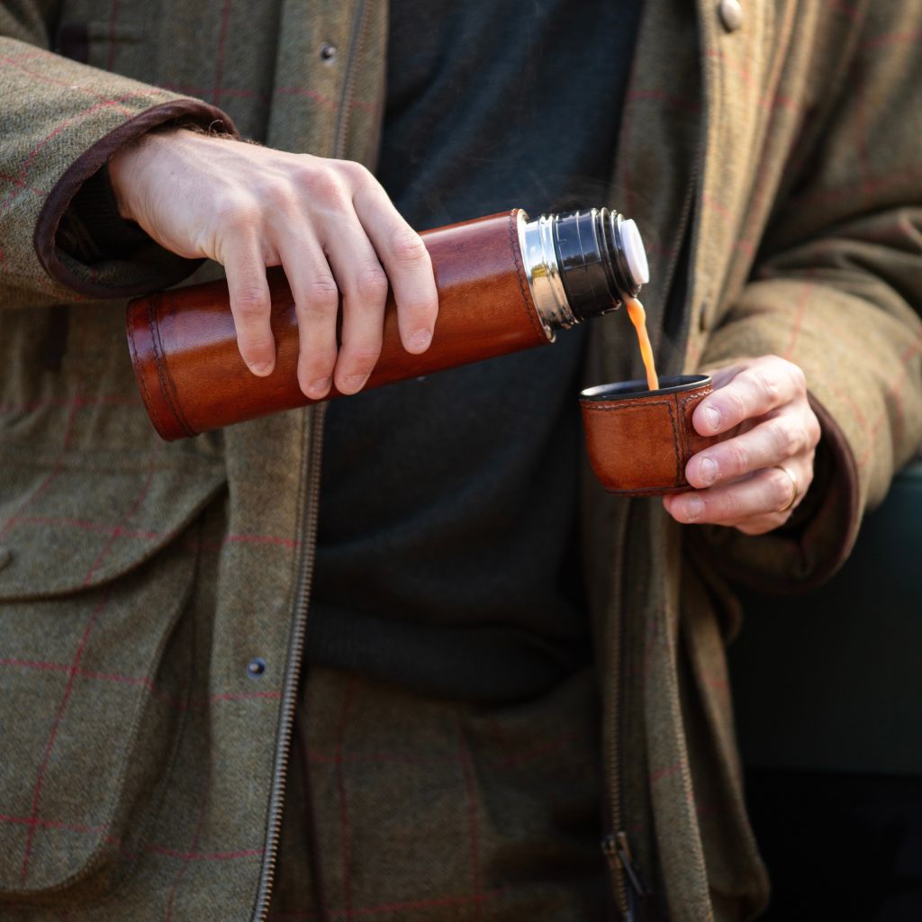 Person pouring a hot drink from leather cased thermos flask