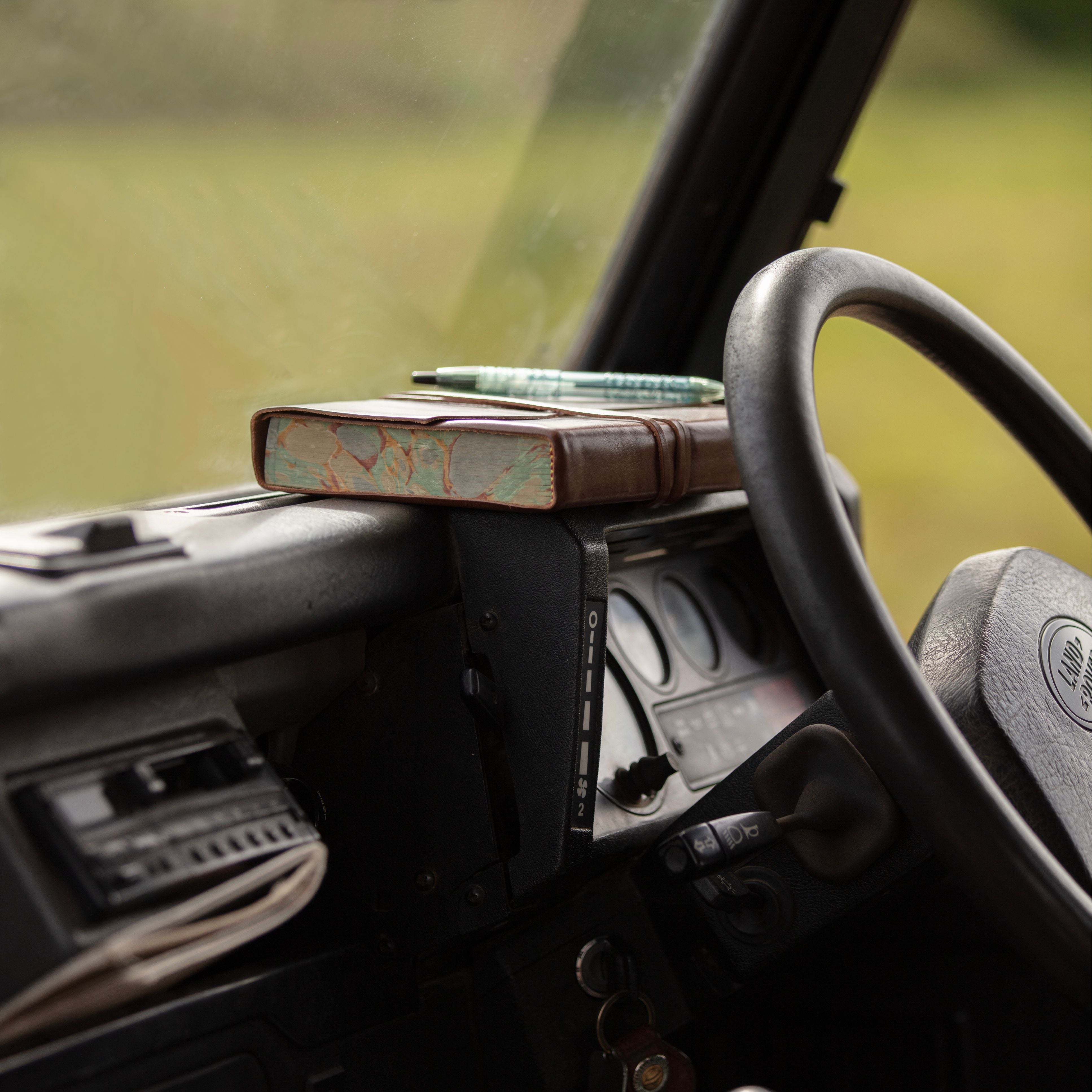 Leather journal with marble edge on a car dashboard with a blurred green landscape outside