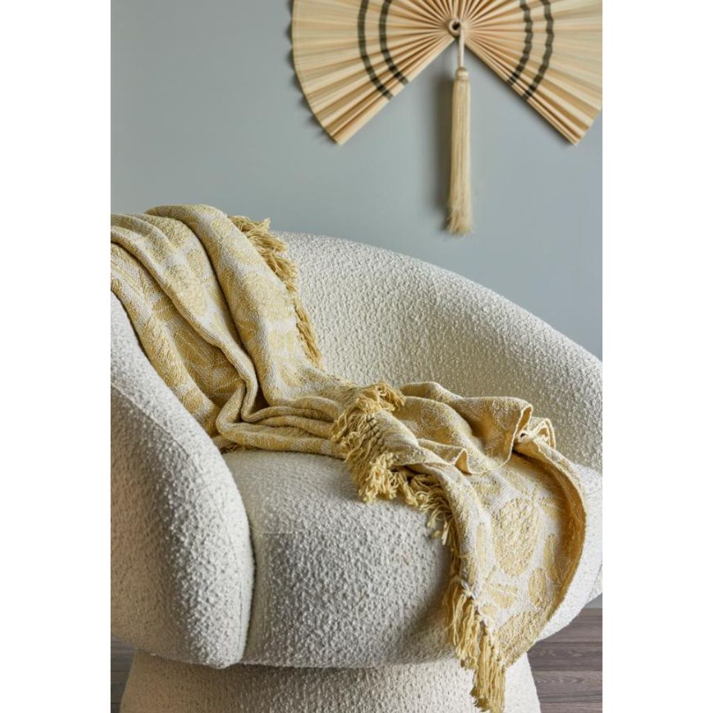 Yellow blanket draped over a textured chair with a decorative fan on the wall.