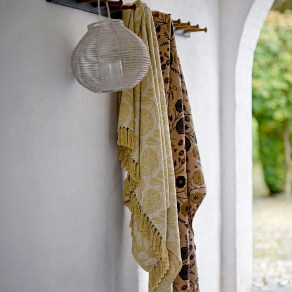 Two patterned scarves hanging on a hook with a lantern above, against a white wall.