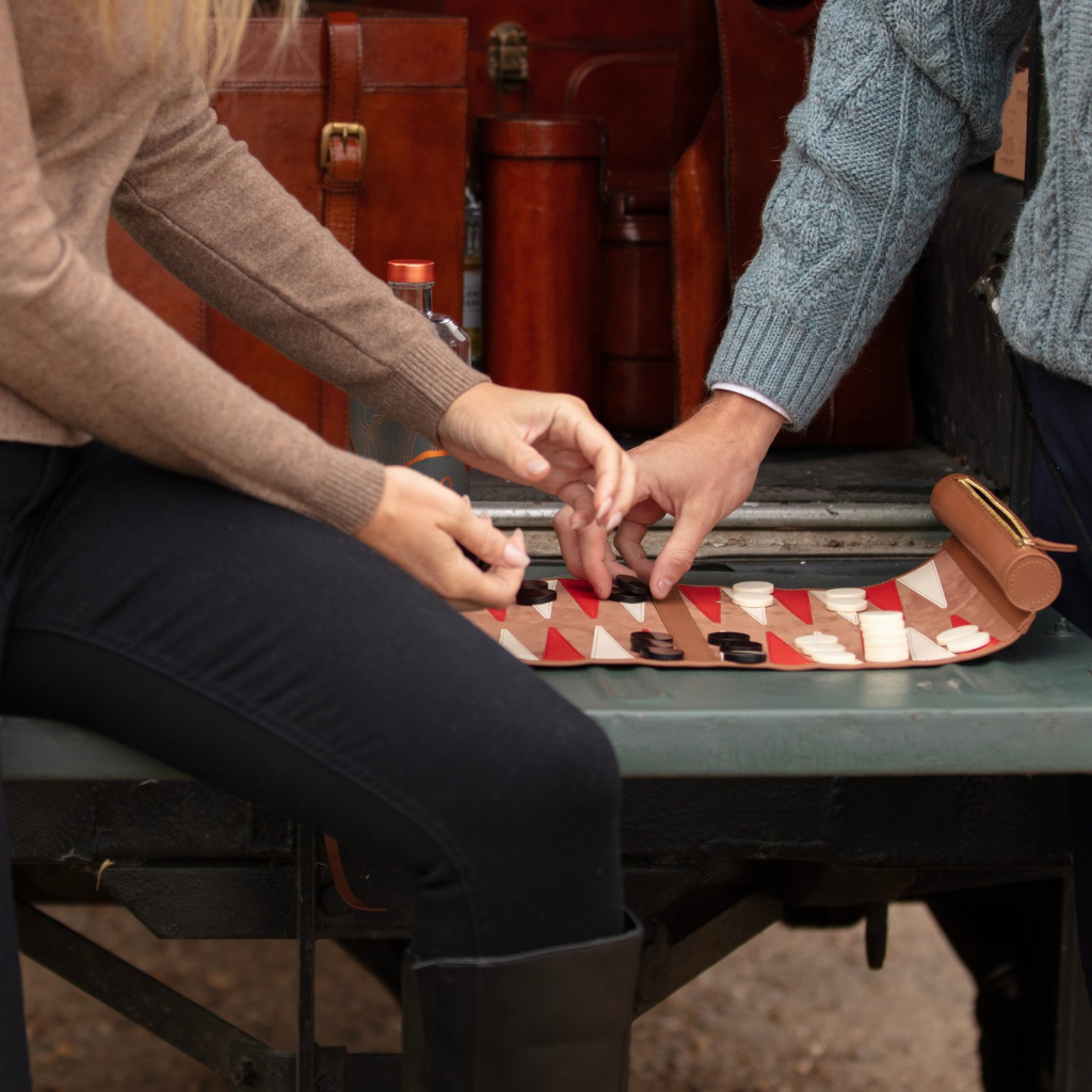 Couple playing a game of travel backgammon on the tailgate of a landrover