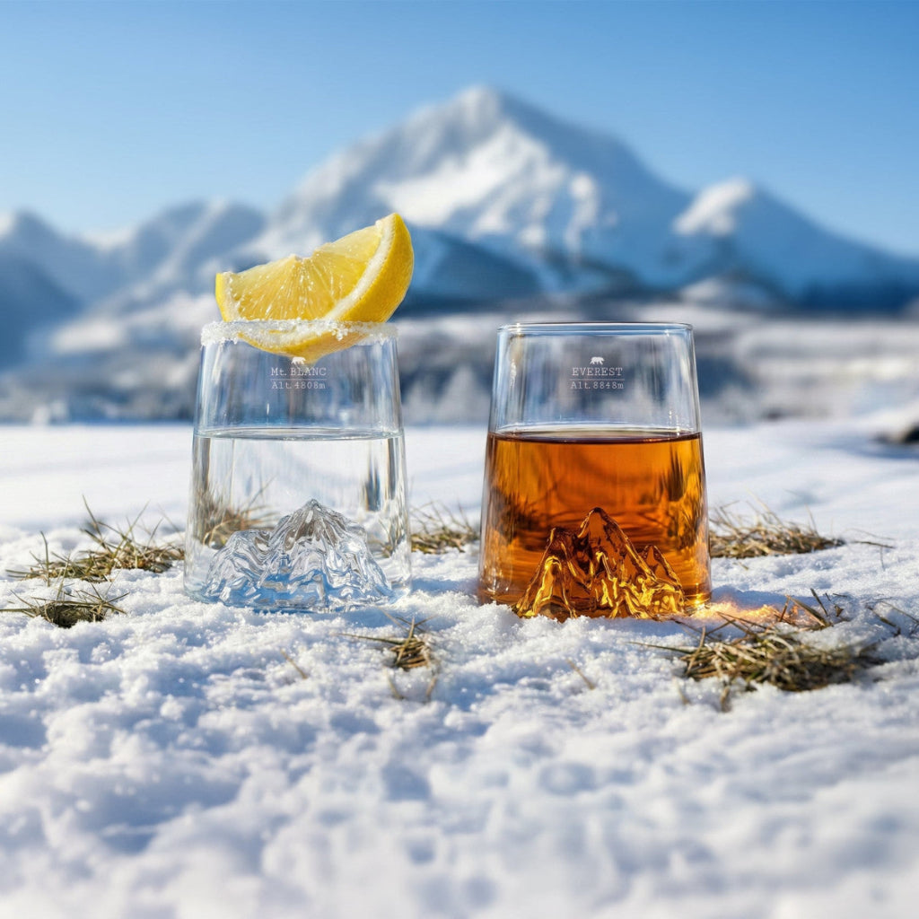 Two glasses on a snowy surface with mountains in the background