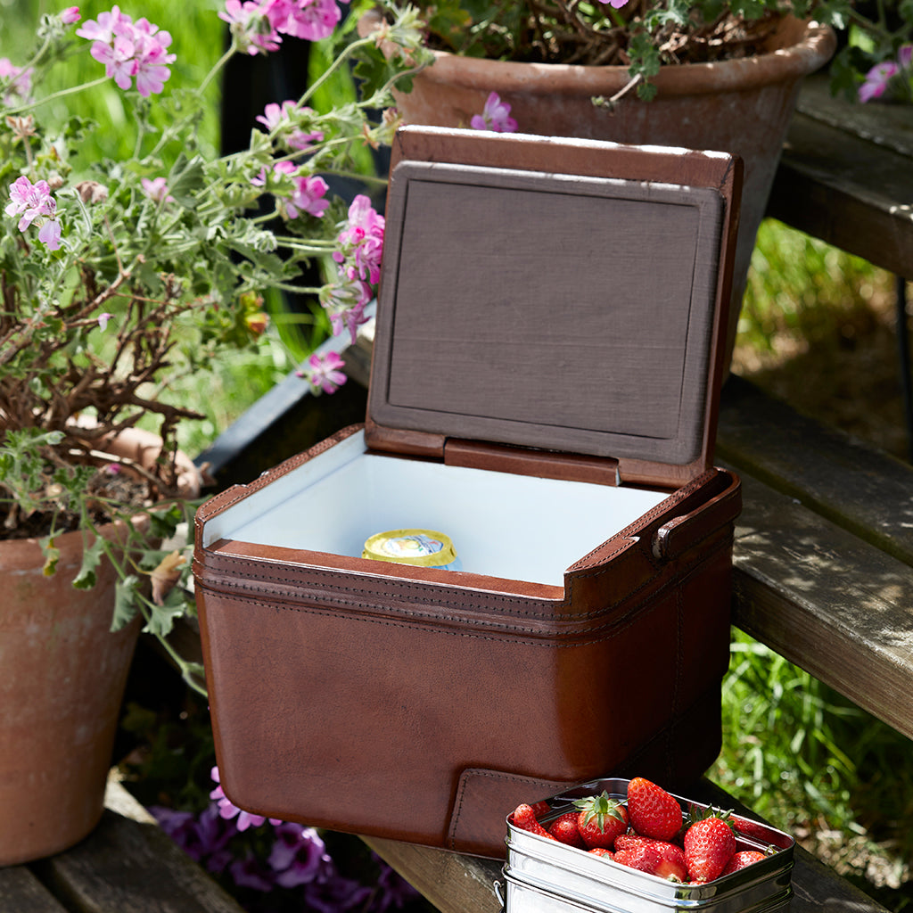Leather cool box open with a can of drink inside  and a pot of strawberries to the side of the  cool box