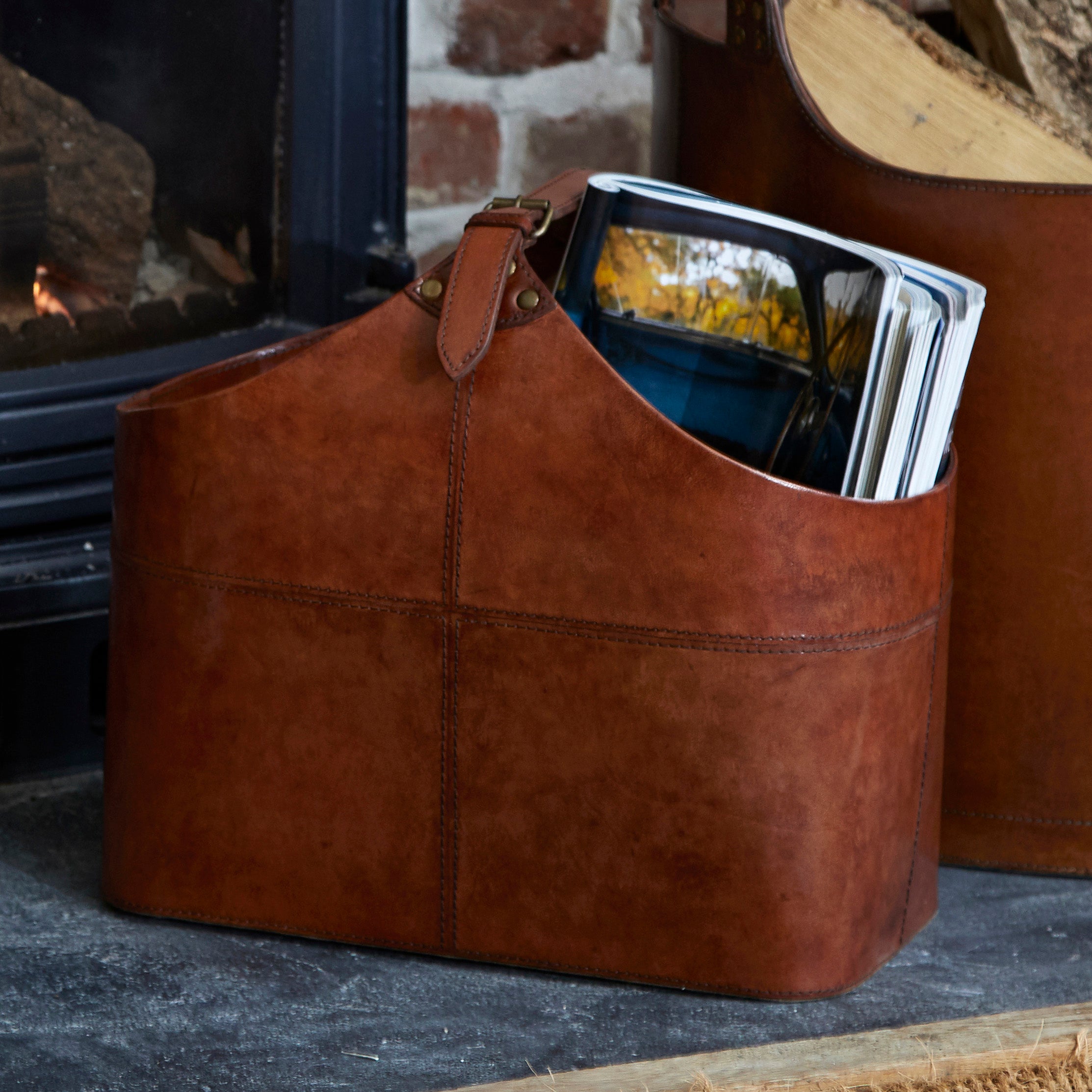 Conker brown leather magazine basket, with magazines in with round log storage basket in background basket 